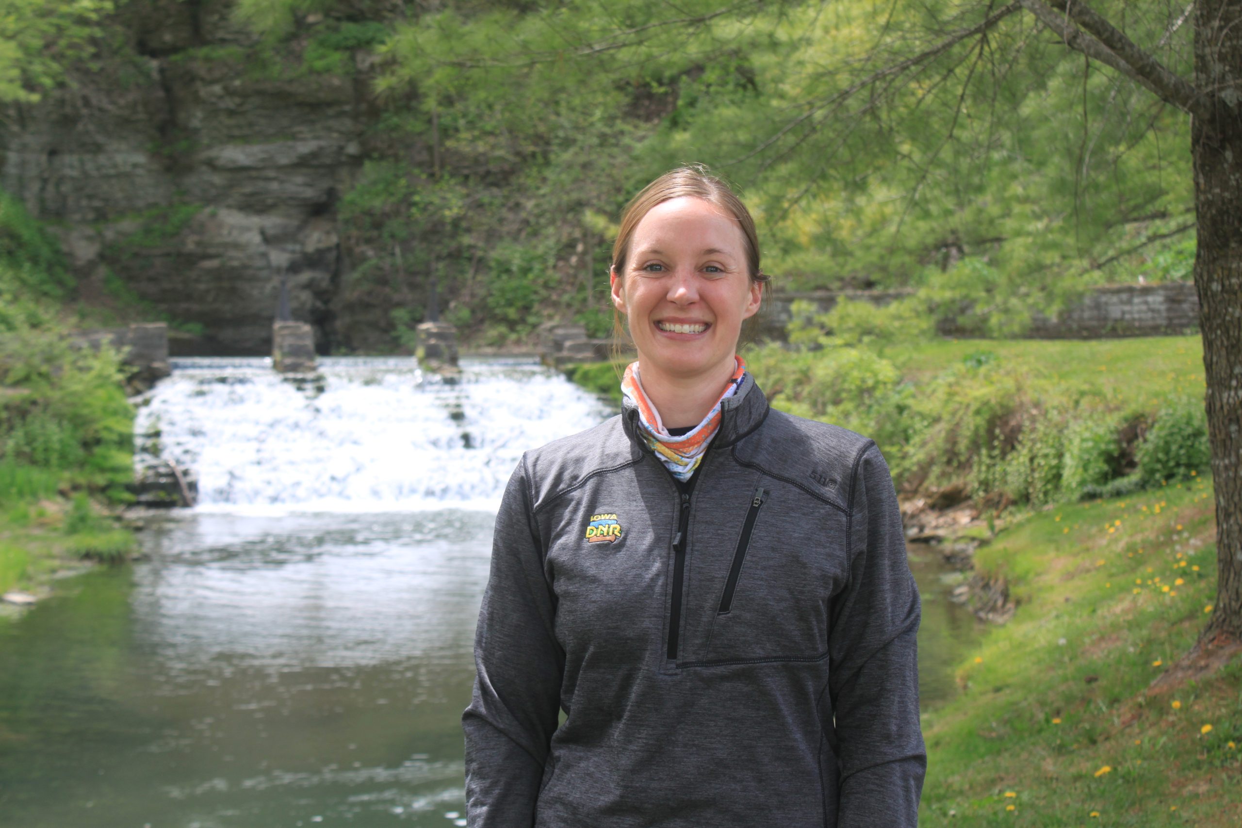 Young woman in a black coat stands in front of water flowing from a spring.