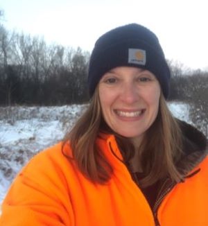 Young lady in stocking cap and blaze orange winter coat standing in snow covered field.