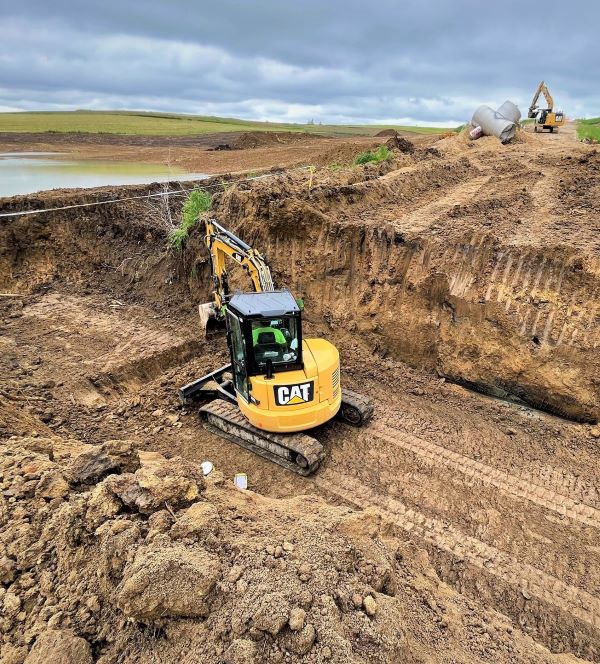 Excavators working in dirt covered landscape with wetland area in background